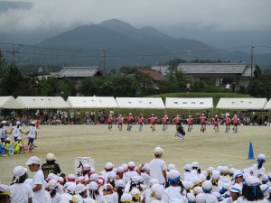 写真：13人の児童が一輪車で一列になり、一糸乱れぬ演技をする様子を見守る児童たち