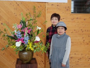 写真：花を生けた地域の先生二人と舞台横に飾られた花