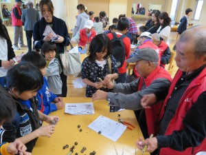 写真:老人クラブの方に楽しそうにどんぐりゴマを教わる児童たち
