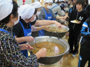 写真：お昼ご飯にトン汁、おもち、さつま芋ご飯に焼きそばを児童によそうスタッフの方たち