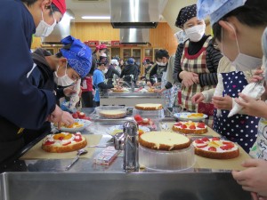 写真：地域ボランティア指導伝承部会の企画でお母さんらに教えてもらいながらケーキを作る児童ら