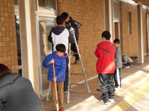 写真：児童たちが協力して脚立を使って校舎の高い所の窓を掃除する様子